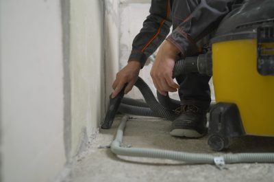 Worker washes the floor with a vacuum cleaner from industrial concrete dust and cement mud during home renovation. A worker vacuums a concrete floor.